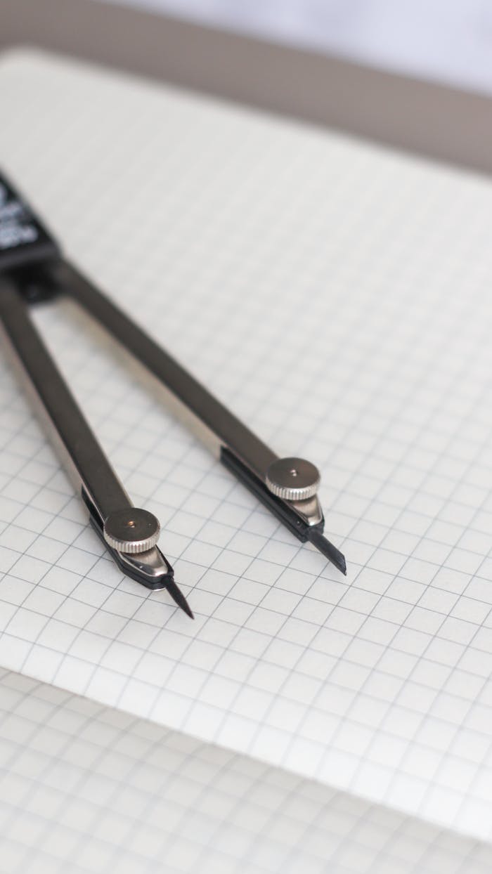 Close-up of a metal drawing compass lying on graphing paper, ideal for technical drawings and design projects.